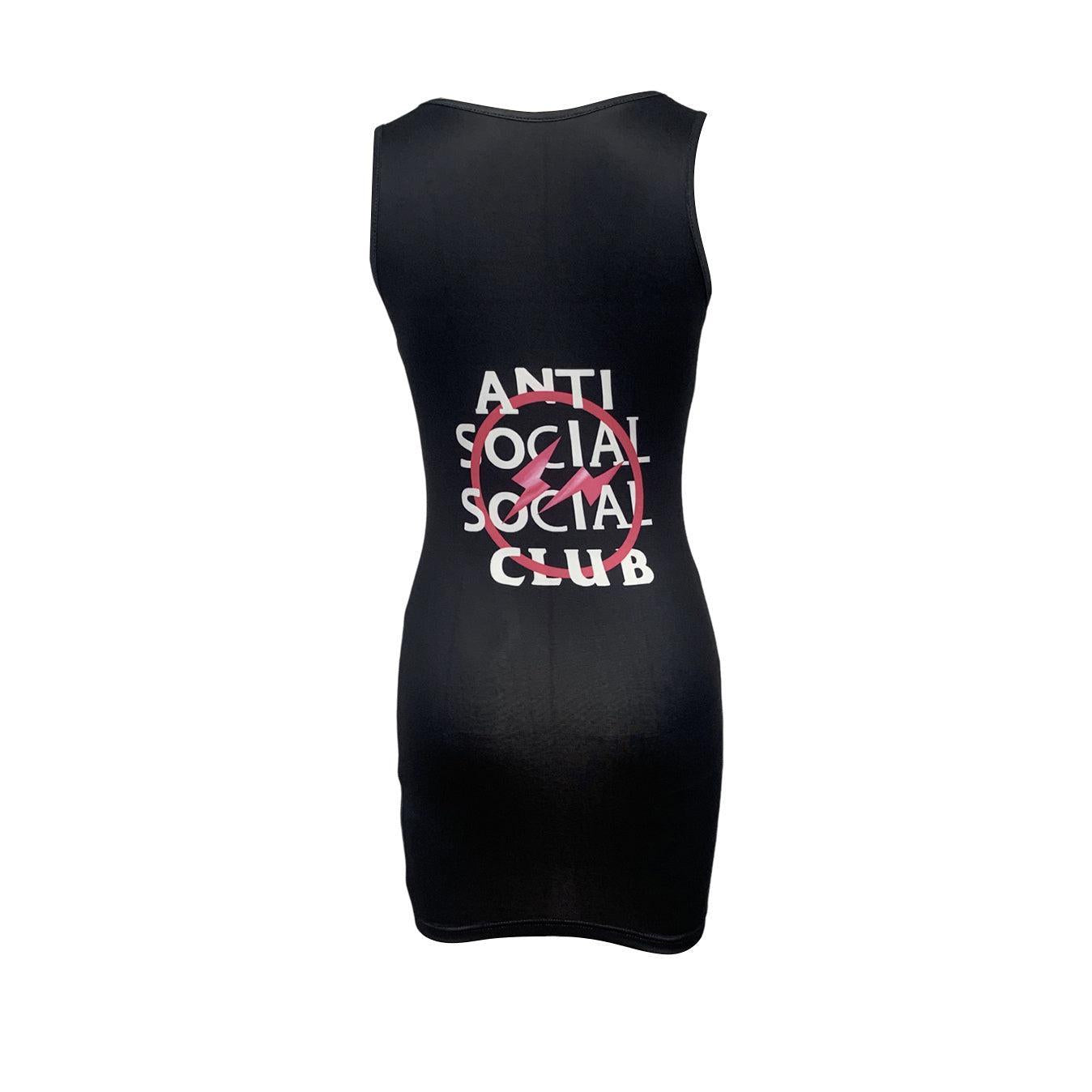 Woman wearing a black sleeveless bodycon dress with "Anti Social Social Club" graphic print on the back, standing by the sea at sunset.