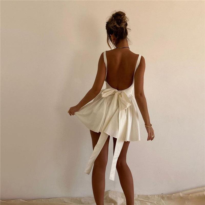 Woman wearing a white mini dress with a square neckline, fitted bodice, and flared pleated skirt, standing against a neutral background.