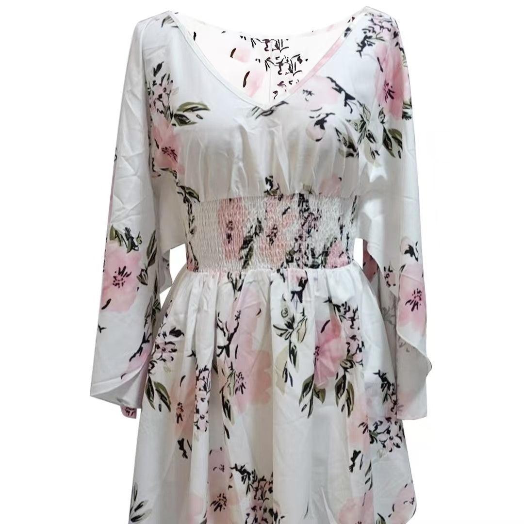 Woman wearing a white floral romper with wide kimono sleeves and pink flower print, featuring a smocked waist and V-neckline.

