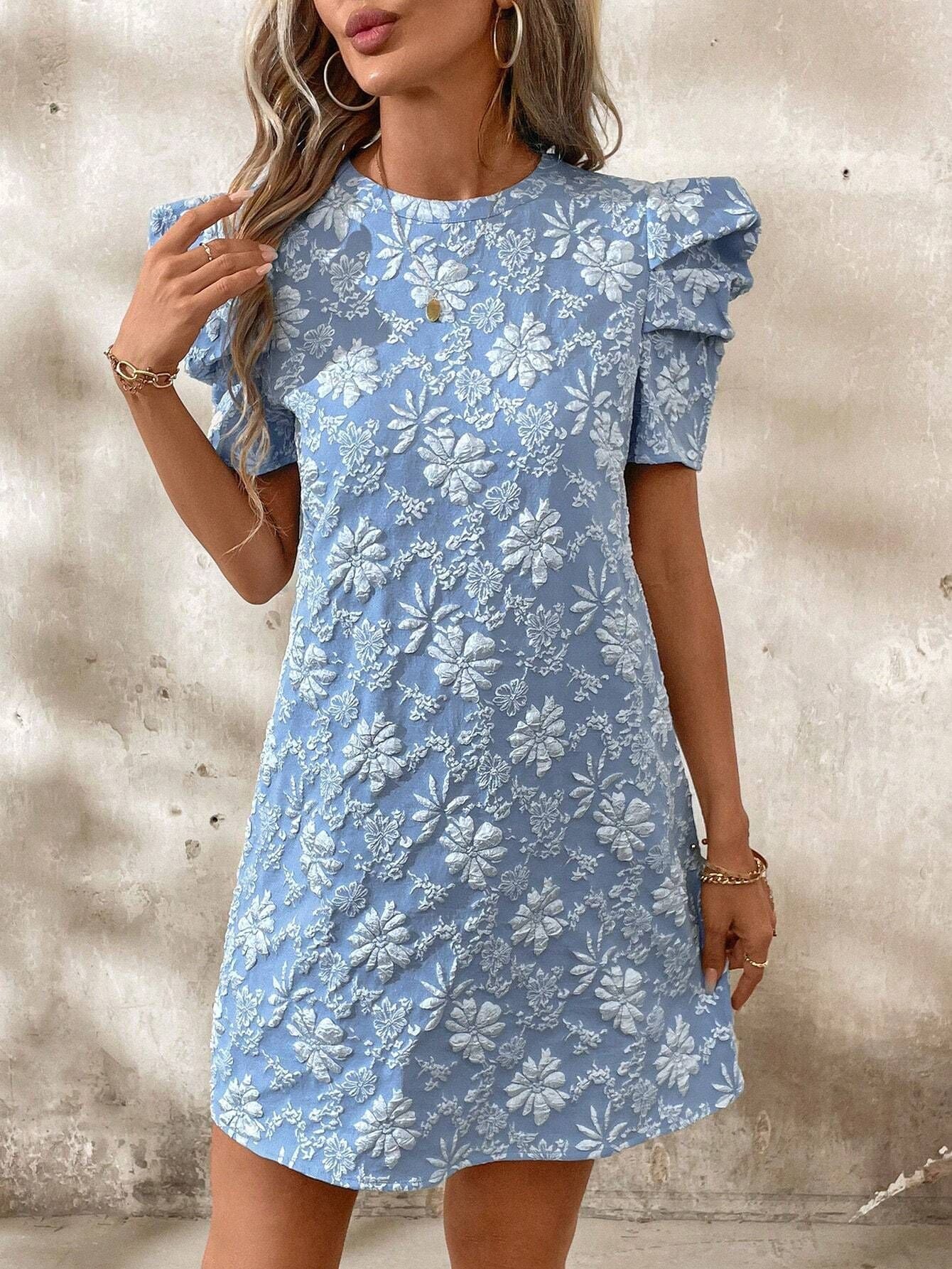 Woman wearing a soft pink mini dress with white floral embroidery and puff sleeves, holding a small white handbag against a neutral background.