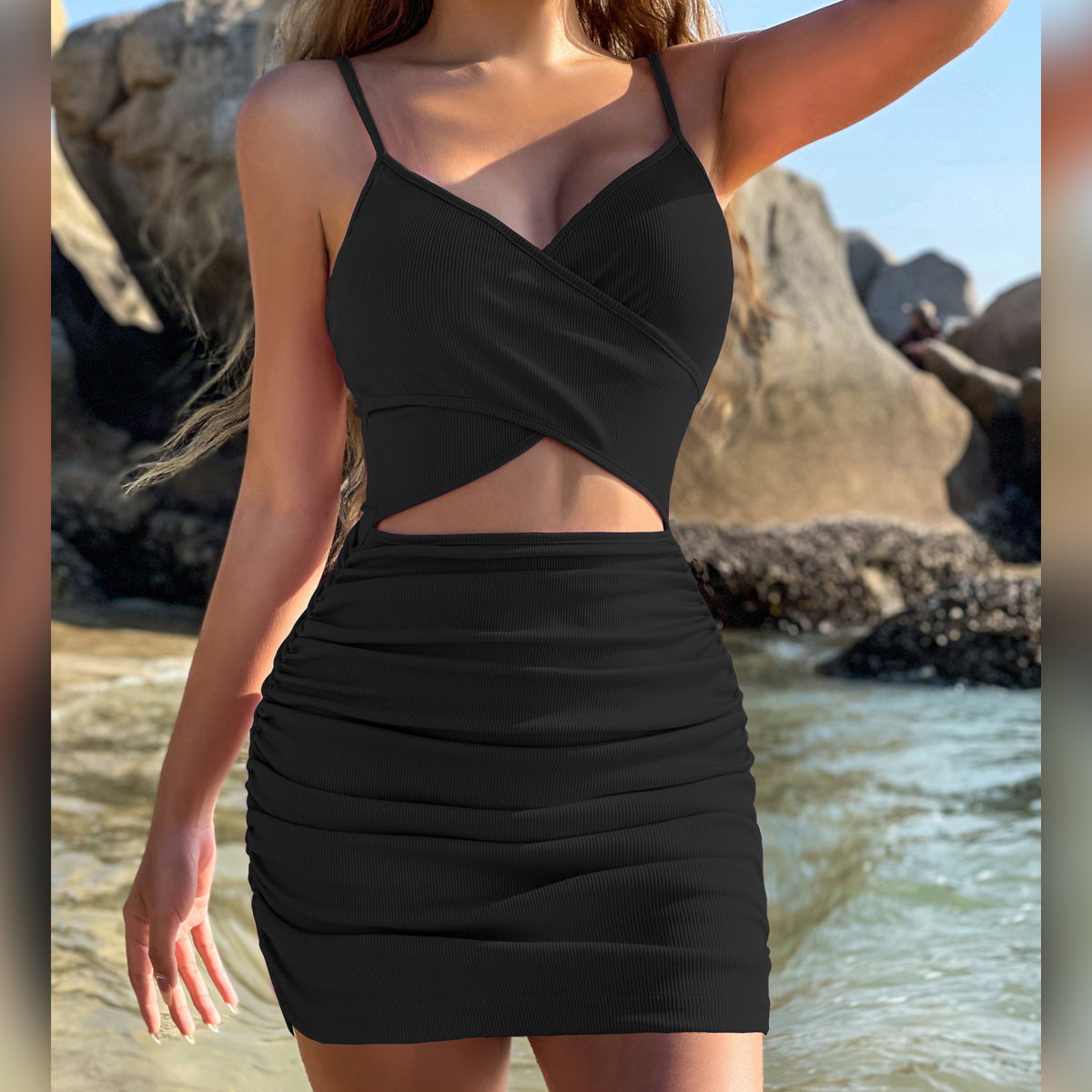 Woman wearing a white bodycon mini dress with a wrap front and side cutout, sitting on beach rocks under the sun.